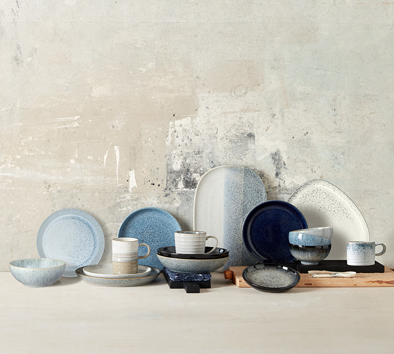 An array of plates, bowls and mugs of various sizes with unique reactive coloured glaze, that have a handcrafted artisan look and feel