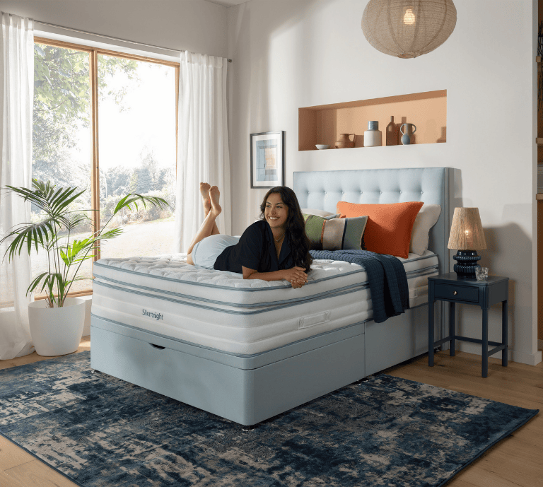 Shows a woman lying comfortably across the Silentnight UltraGel 3500 mattress on a blue divan base. 