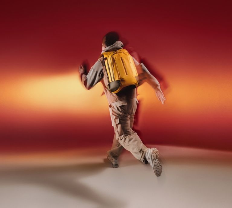 man running with yellow backpack on and orange background