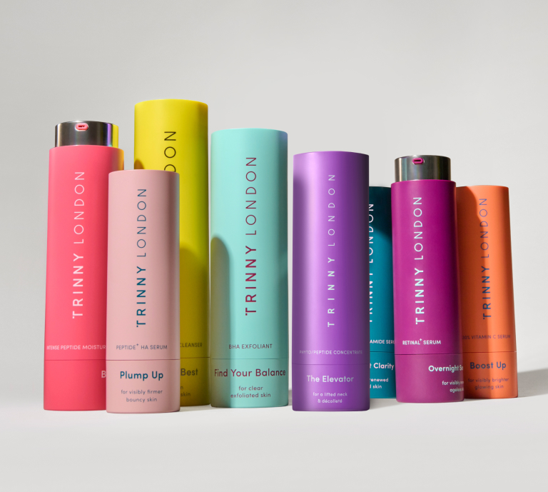 An image of Trinny London's full skincare range, showing all the multi-coloured product packaging against a grey studio background.